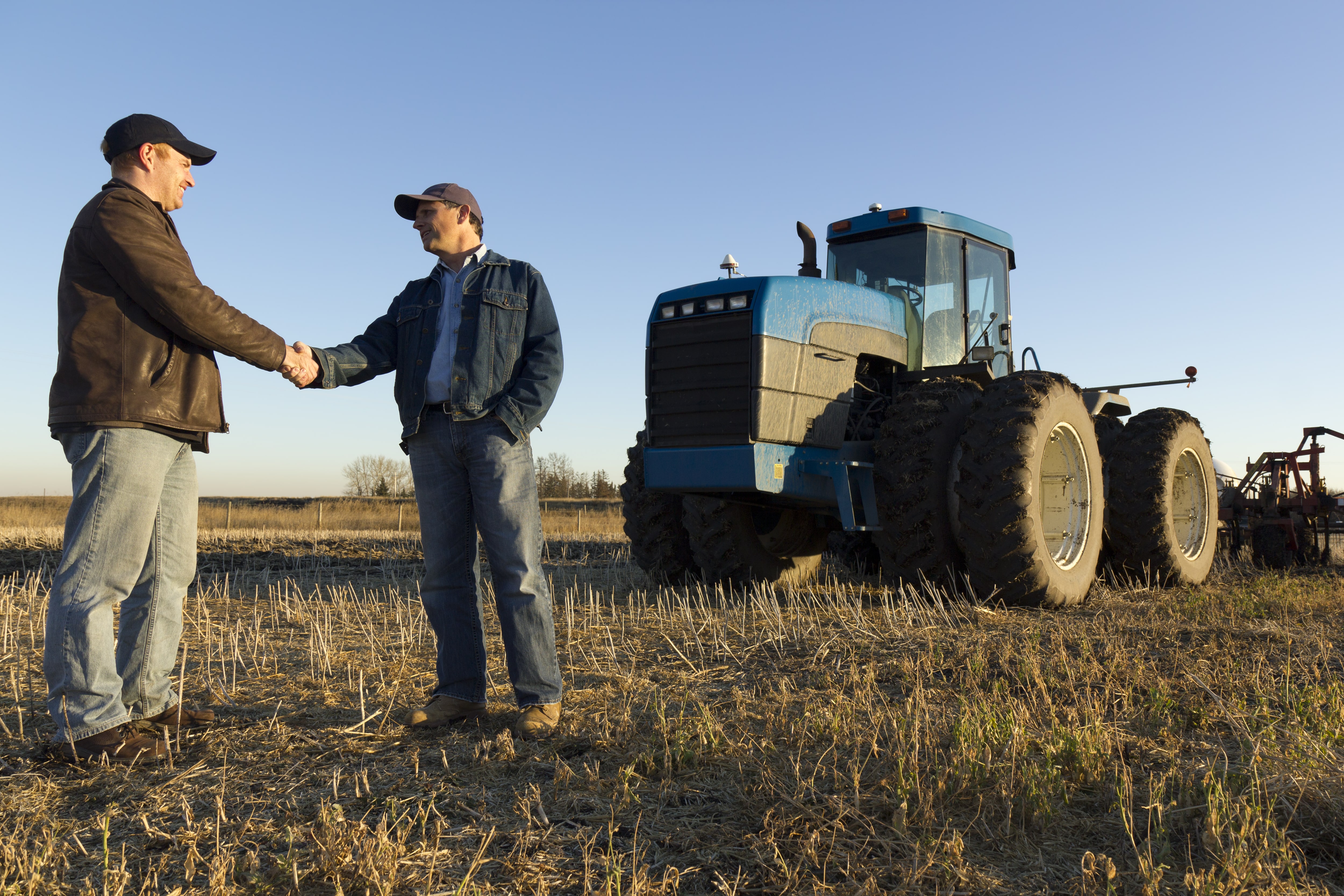 Two persons shaking hands in a field in front of a tractor